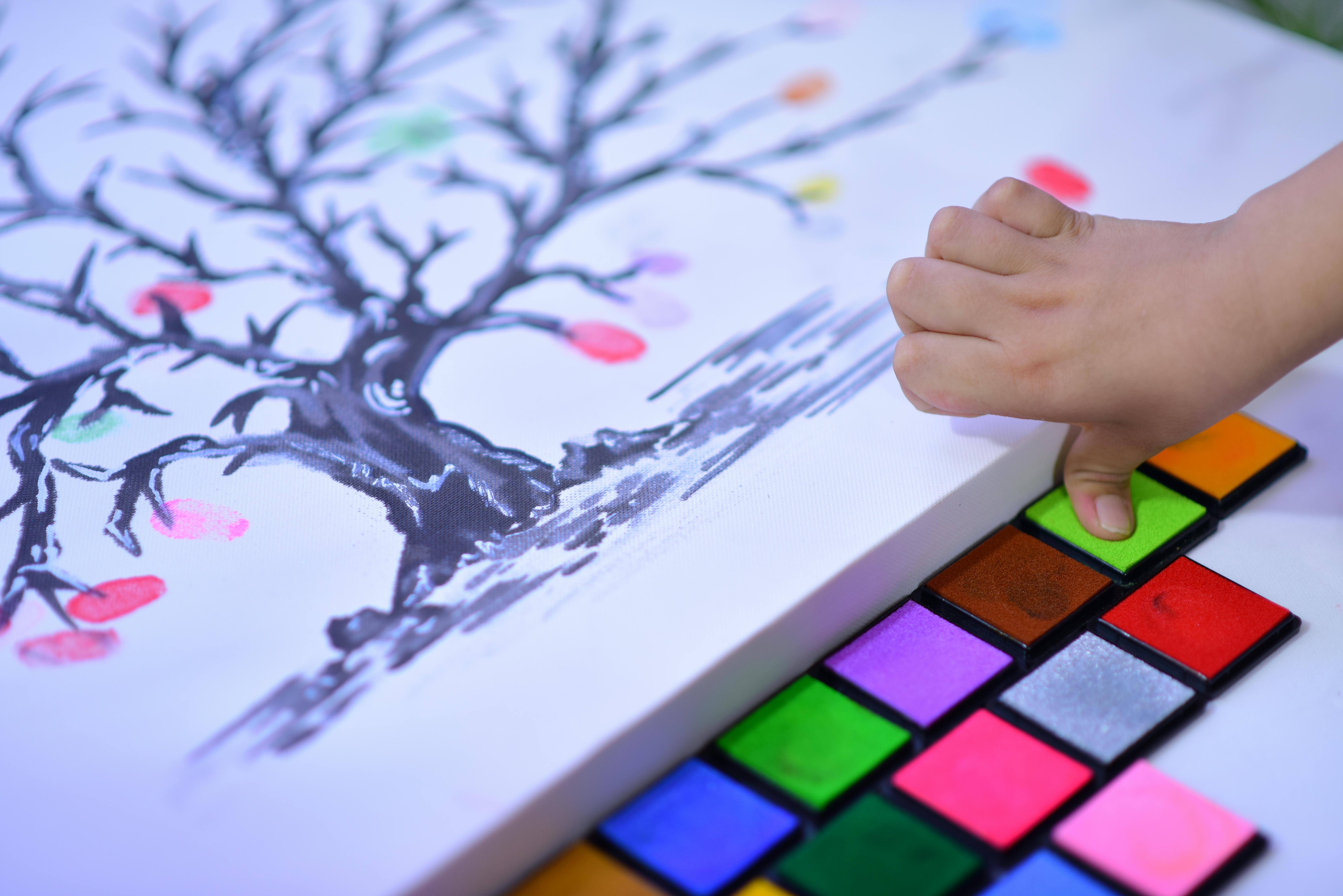 Close-up of a child's hand painting with vibrant colors on a tree canvas.